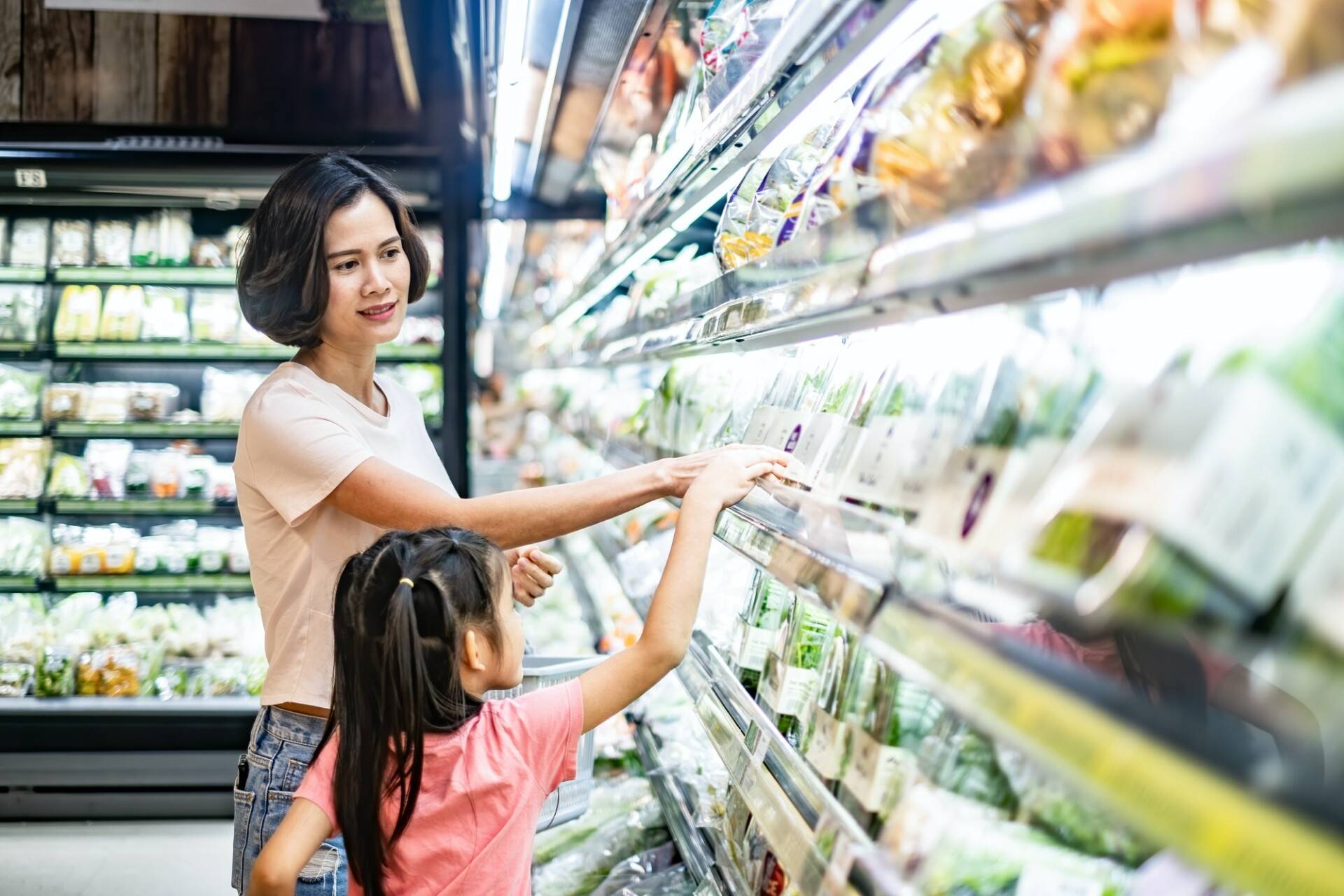 Young Asian beautiful mother holding grocery basket with her child walking in supermarket.